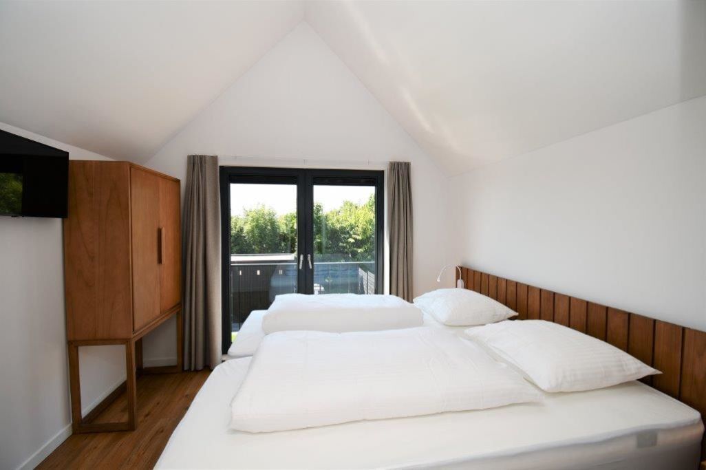 A bedroom with a large bed, wooden wardrobe, and a view through a window.