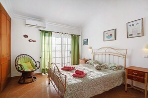 Um quarto com cama, uma poltrona de balanço, mesa de cabeceira e guarda-roupa.