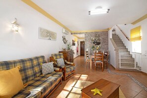 Uma sala de estar com sofá, poltronas, mesa de centro, escada e espaço para refeições.