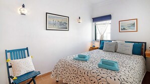 Ein Schlafzimmer mit einem Bett, einem Sessel, einem Nachttisch und Wandleuchten.