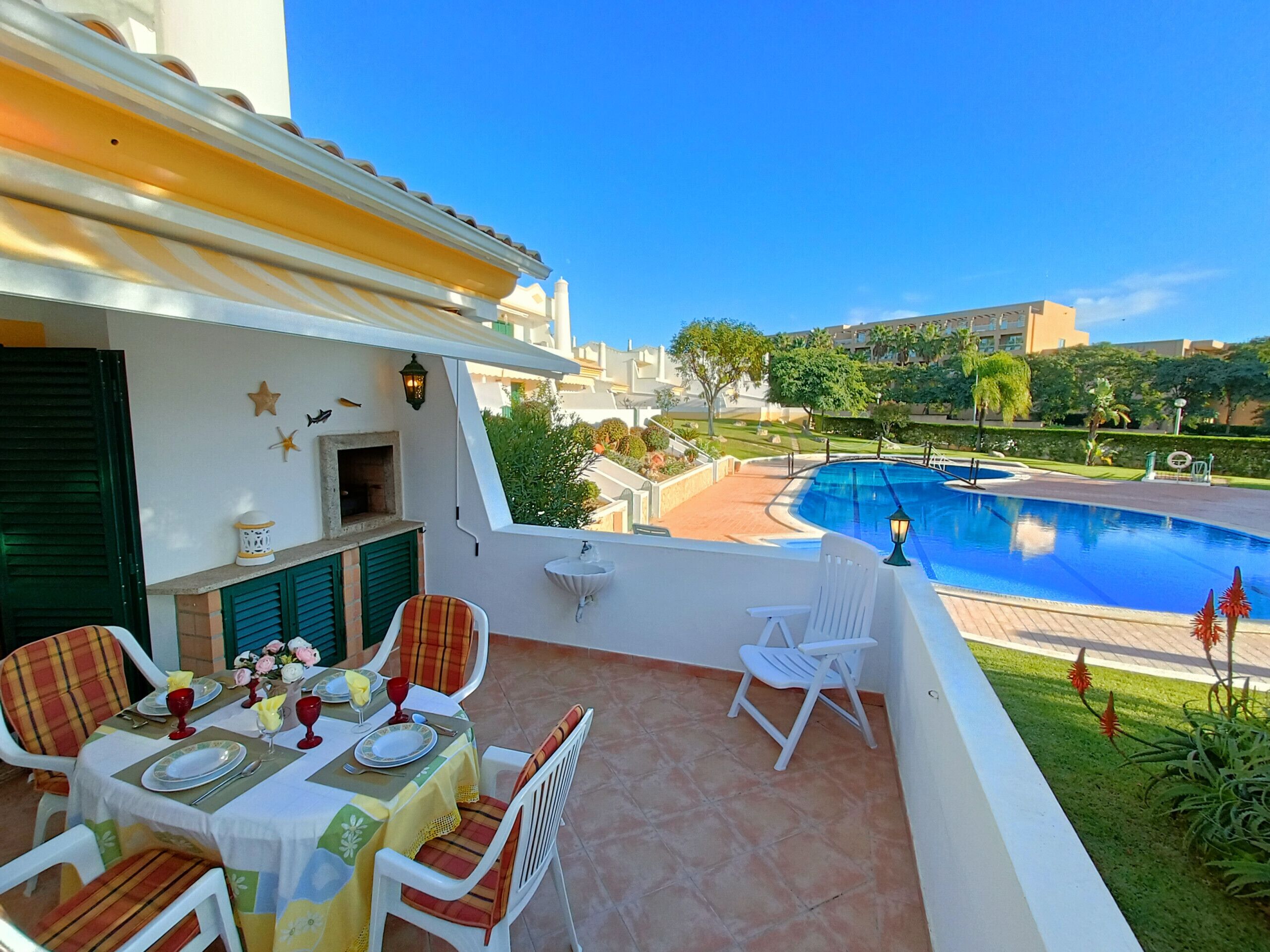 A terrace with a dining table set for two, a pool, and a view of the surrounding area.