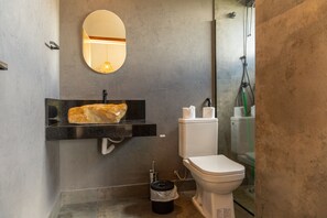 A modern bathroom with a granite sink, a toilet, and a glass shower enclosure.