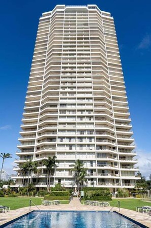 A high-rise hotel with multiple balconies, a swimming pool, and a well-maintained lawn.