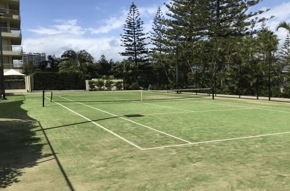 A tennis court with a net, surrounded by trees and a building. - Contessa Queen - Main Beach (Gold Coast)