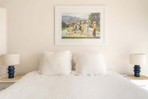 A bedroom with a bed, two bedside lamps, and a framed picture on the wall.