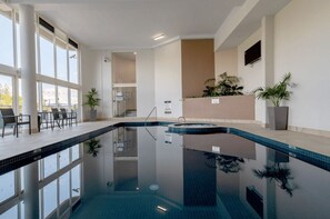 Une piscine intérieure avec des parois en verre transparent, un espace détente avec des fauteuils et des plantes en pot.