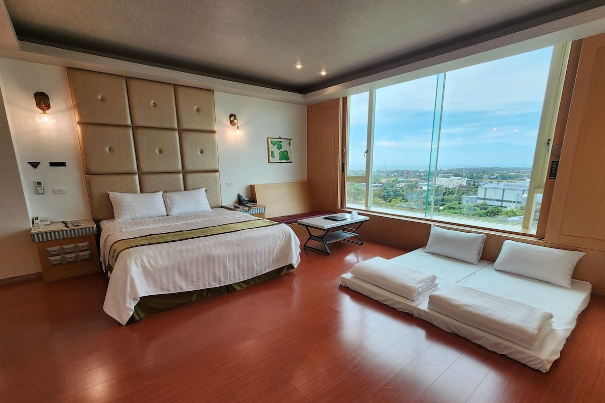 Habitación de hotel con una cama grande, un sofá, una mesita y un ventanal con vistas a la ciudad.