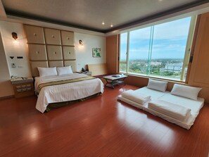 A hotel room with a large bed, a sofa, a small table, and a large window offering a city view. - I need motel (Xinfeng)