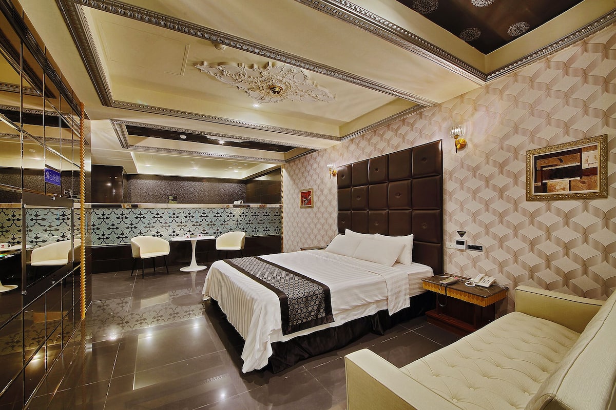 Una habitación de hotel moderna con una cama grande, una mesita de noche, una silla y un espejo.