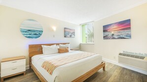A bedroom with a bed, a nightstand, a wall-mounted heater, and three framed pictures depicting ocean scenes. - Pelican Pointe 325:Walk to Beach~Pool~Free Parking (Clearwater Beach)