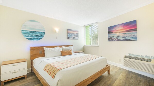 Une chambre à coucher comprenant un lit, une table de chevet, un radiateur fixé au mur et trois tableaux représentant des scènes maritimes.