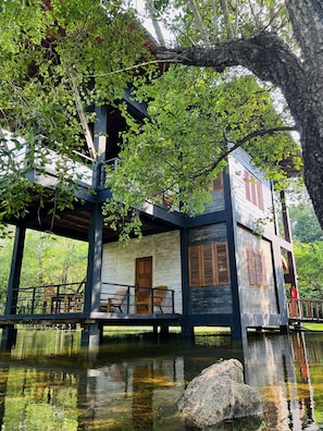 A wooden house with a balcony, situated over a body of water, surrounded by trees. - Sigiri Vananthara  (Habarana)