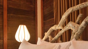 Una cama con ropa blanca y una lámpara sobre una mesita de noche de madera.
