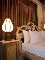 Una cama con ropa blanca, un cabecero de madera con diseño de rama natural y dos lámparas sobre mesitas de noche.