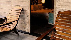 Una habitación de madera con una cama, una mesita de noche y una lámpara. Hay dos sillas de madera.
