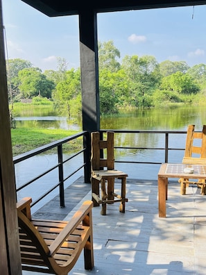 Una terraza de madera con una mesa y sillas que da a un cuerpo de agua y follaje.