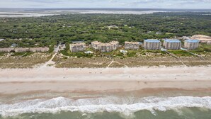 Une station balnéaire dotée de villas en bord de mer, d’une plage de sable et d’une forêt dense en arrière-plan.