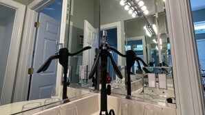 Et badeværelse med et stort spejl, en vaskepult med håndvask og en lampe på stativ.