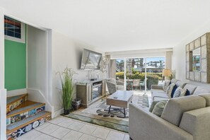 A living room with a sofa, coffee table, and a TV mounted on the wall. - Seaspray Condos - 100A (Fort Walton Beach)
