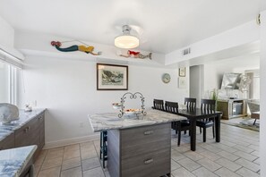 A modern kitchen with a marble countertop, dark wooden dining table, and chairs. - Seaspray Condos - 100A (Fort Walton Beach)
