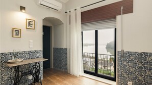 A room with a wooden table, a bench, a view of a lake, and patterned walls. - Casa Curva do Rio (Melres)