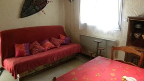 Una habitación con un sofá rojo, una mesa pequeña con mantel rojo y una ventana con vistas.