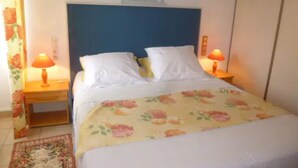 Un dormitorio con cama, dos lámparas de noche, colcha con estampado floral y cabecera con la palabra “bonheur”.