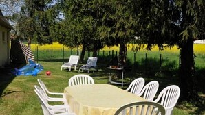 Un área de comedor al aire libre con mesa y sillas, rodeada de árboles y una cerca.