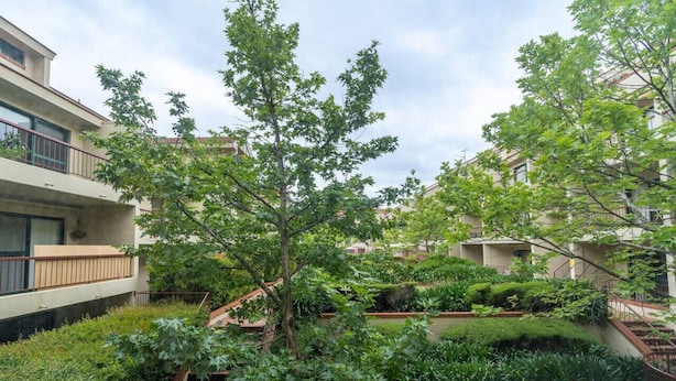 Edifício residencial com várias varandas, um pátio central com uma árvore e uma escadaria que dá acesso aos andares superiores.
