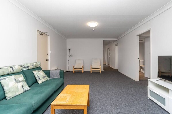 Une pièce avec un canapé vert, deux fauteuils, une table basse en bois et un meuble pour la télévision.