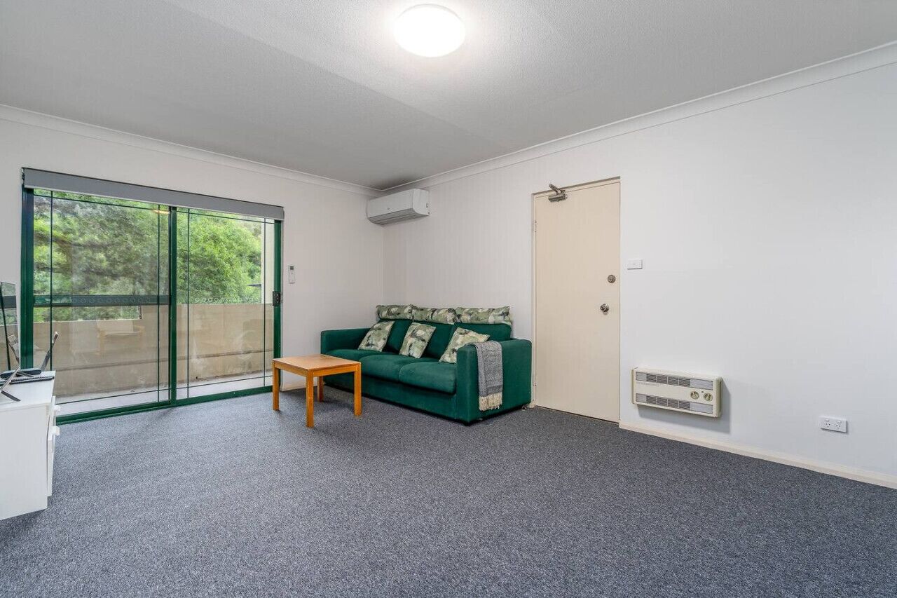 A room with a green sofa, a small wooden table, a sliding glass door, and a white door.