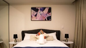 Ein Hotelzimmer mit einem großen Bett, zwei Nachttischen, einem an der Wand hängenden abstrakten Gemälde und einem Fenster mit Vorhängen.