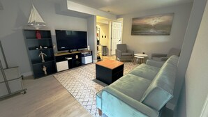 A modern living room with a flat-screen TV, a light blue sofa, a wooden coffee table, and a patterned rug. - SeaSide Serenity - Cozy Retreat on Bay Drive (Kill Devil Hills)