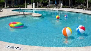 Ein Pool mit Liegestühlen und Palmen, umgeben von einem Gebäude mit Balkonen.
