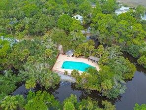 An aerial view of a private property with a swimming pool surrounded by dense tropical vegetation and a small house.