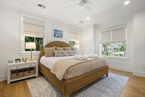 A bedroom with a large bed, a nightstand, a lamp, and a view of greenery outside.
