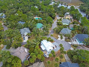 An aerial view of a residential area with houses surrounded by dense greenery and a small body of water.