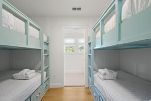Une pièce avec des lits superposés, une porte donnant sur une autre pièce et une fenêtre avec vue sur la verdure.