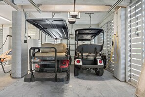 Two golf carts parked inside a garage with concrete pillars and a metal door.