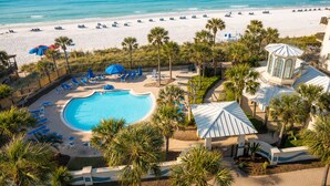 Een resort met een zwembad, ligbedden en palmbomen.