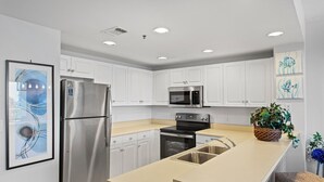 Een moderne keuken met witte kastjes, roestvrijstalen apparatuur, een beige aanrecht en een spoelbak.