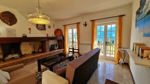 A cozy living room with a fireplace, a sofa, a dining table, and a view of the outdoors through large windows. - Country House Casa Marisa Balcony lake view (Tremosine)