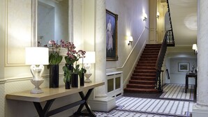 A grand hallway with a large mirror, a console table with lamps and vases, a patterned carpet, and a staircase leading to another level. - Cheval Hyde Park Gate (London)