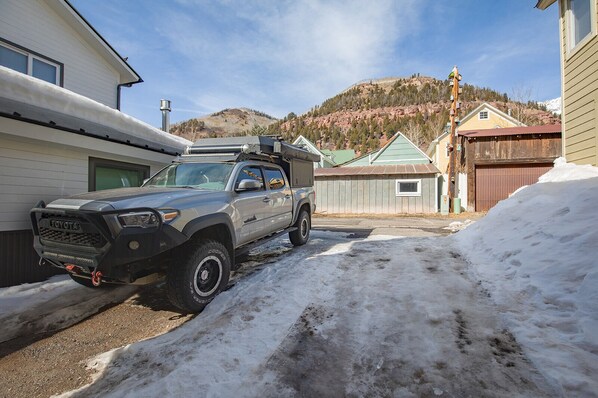 A gray pickup truck parked in a snowy driveway with houses and a mountain in the background. - Pac. Street Style: In-Town 1bdrm (Telluride)