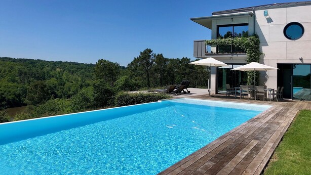 Ein modernes Haus mit Swimmingpool, Gartenmöbeln und Blick auf den Wald.
