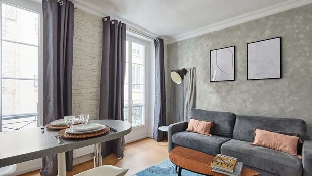 A modern living room with a grey sofa, a round coffee table, and a dining table with plates and glasses. - Apartment  Center of Paris (Paris)