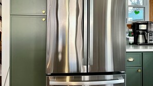 Un réfrigérateur en acier inoxydable dans une cuisine avec des meubles de couleur verte et une fenêtre.