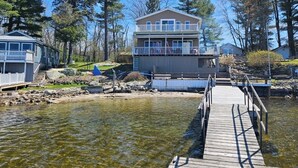 Une propriété située au bord de l’eau, avec une jetée en bois menant à une maison dotée d’un balcon.