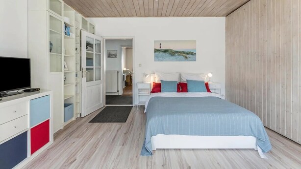 A bedroom with a bed, a TV, a wardrobe, and a painting on the wall.