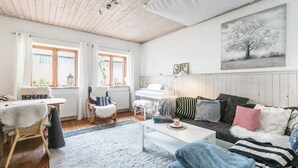 A cozy living room with a wooden ceiling, a white piano, a sofa with striped cushions, and a painting of a tree.
